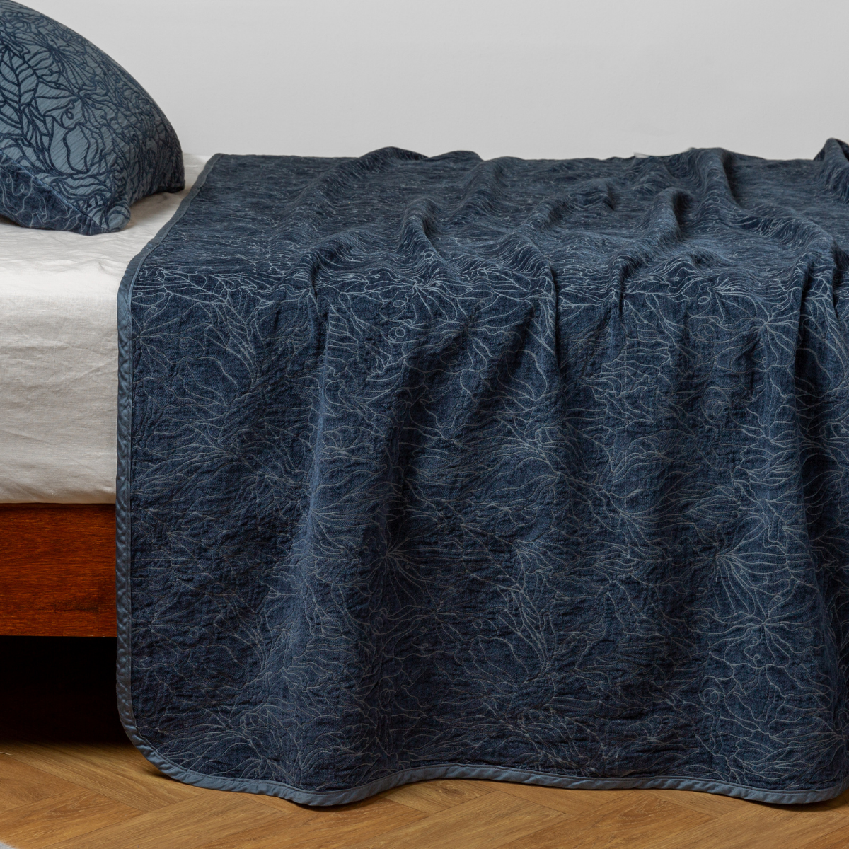 Midnight Georgia bedspread draped over bed edge, showing quilted botanical pattern detail.
