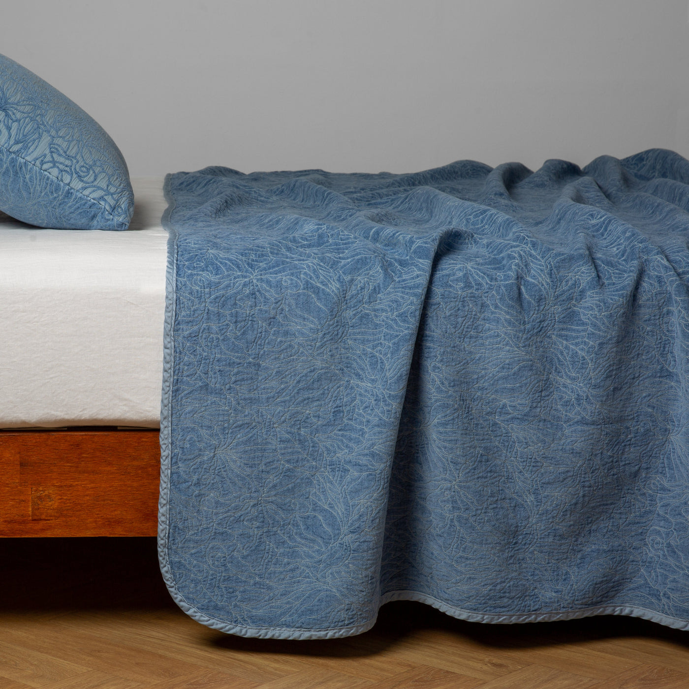 Bella Notte Georgia bedspread in Tahoe Blue draped over bed, showing quilted floral texture.