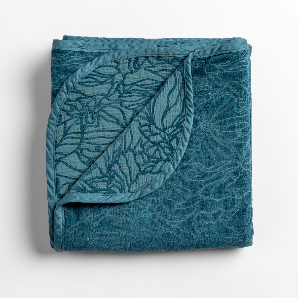 Folded Cenote blanket with corner turned back showing quilted floral pattern on velvet fabric.