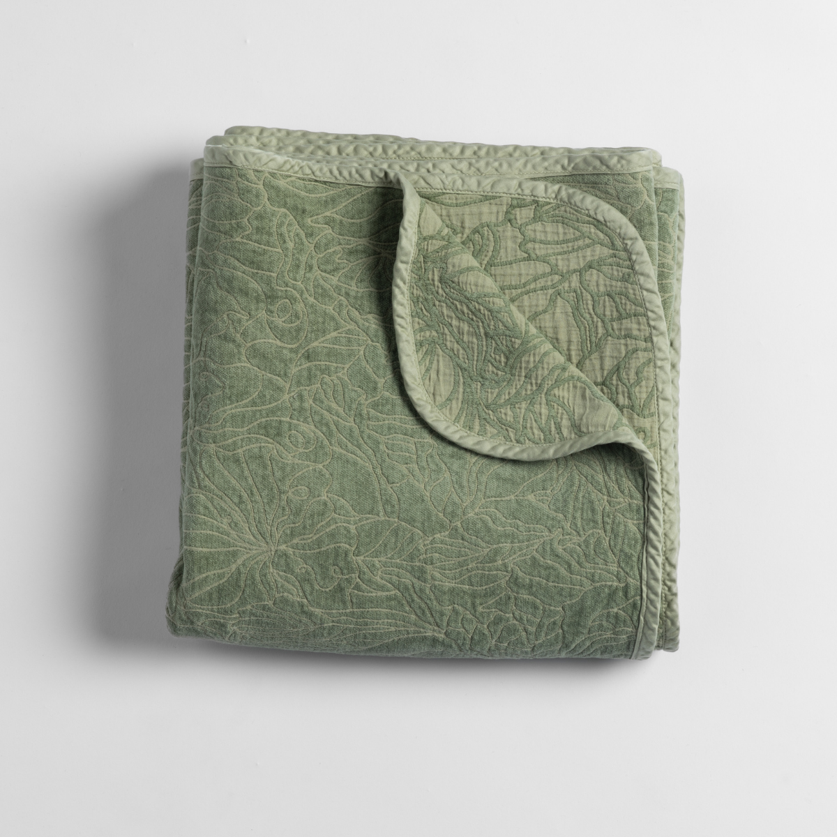Desert Sage Georgia blanket folded, showing quilted botanical leaf pattern and corded trim detail.