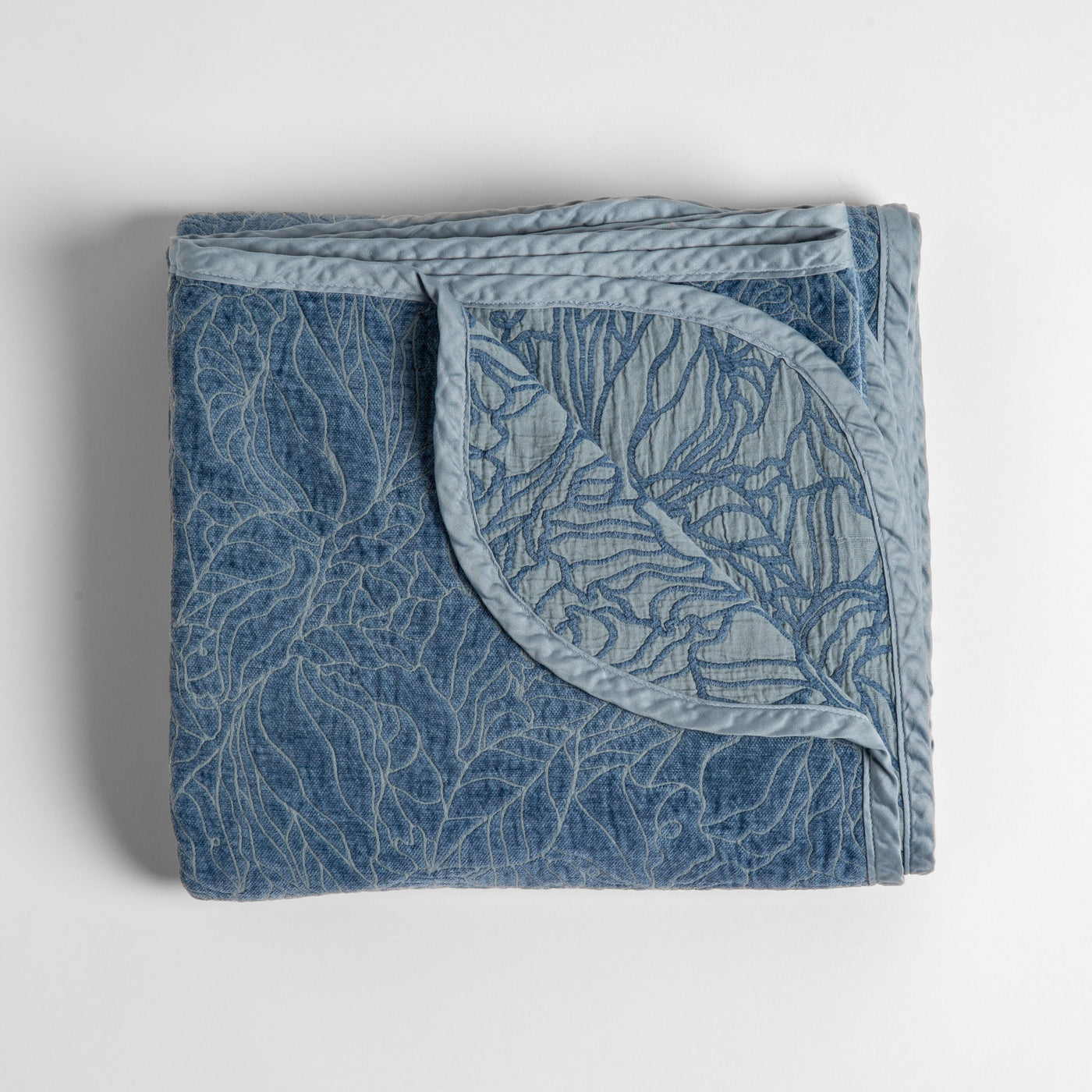 Bella Notte Georgia blanket in Tahoe Blue, folded showing quilted botanical pattern and contrast border.