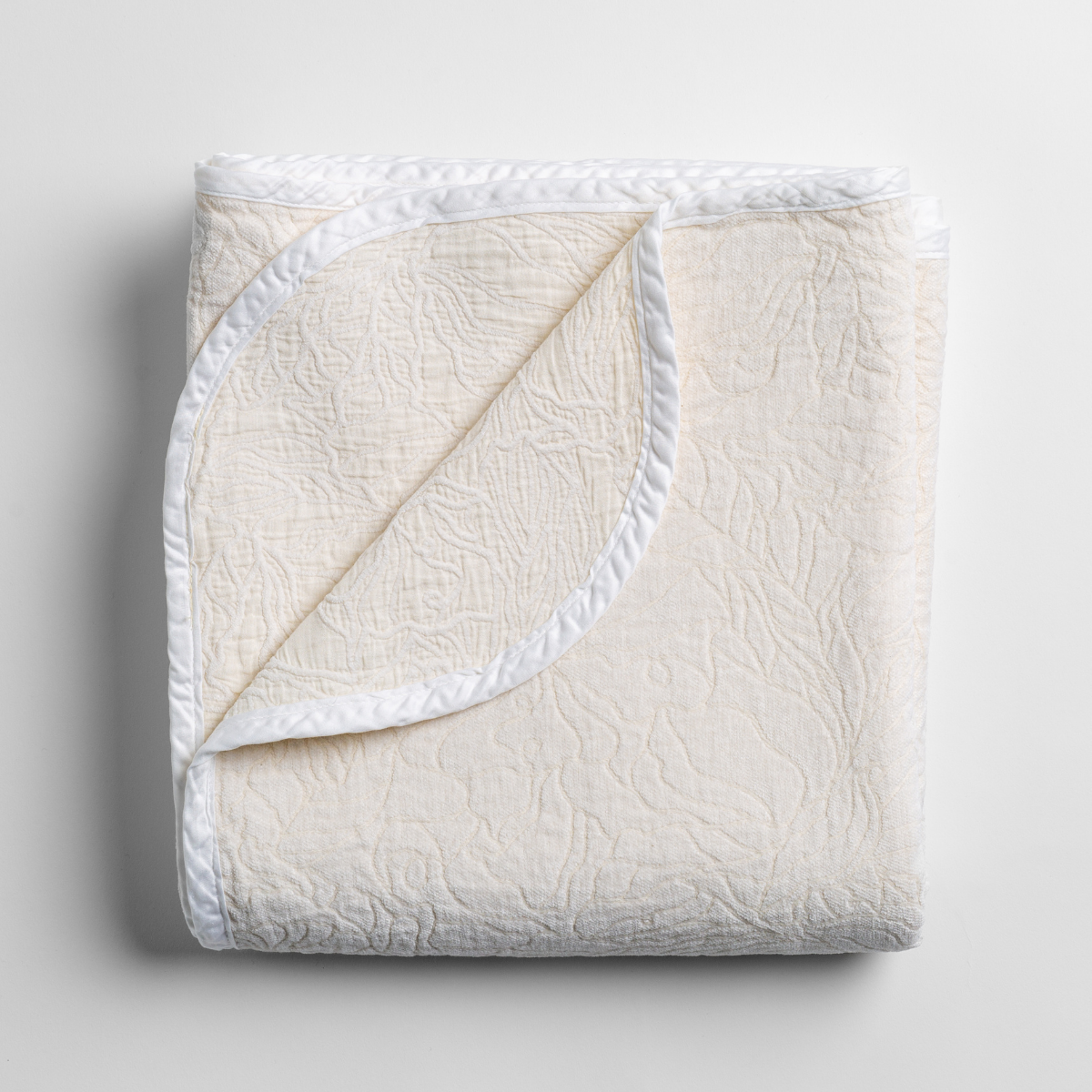 Bella Notte Georgia blanket in Winter White, folded flat showing quilted texture and satin trim.