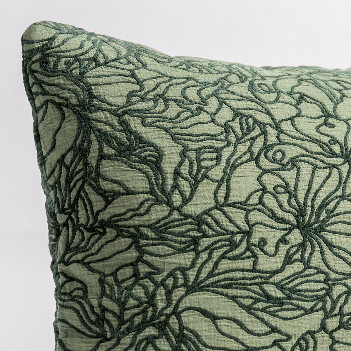 Close-up of dark Juniper floral embroidery stitching on a sage linen throw pillow corner.
