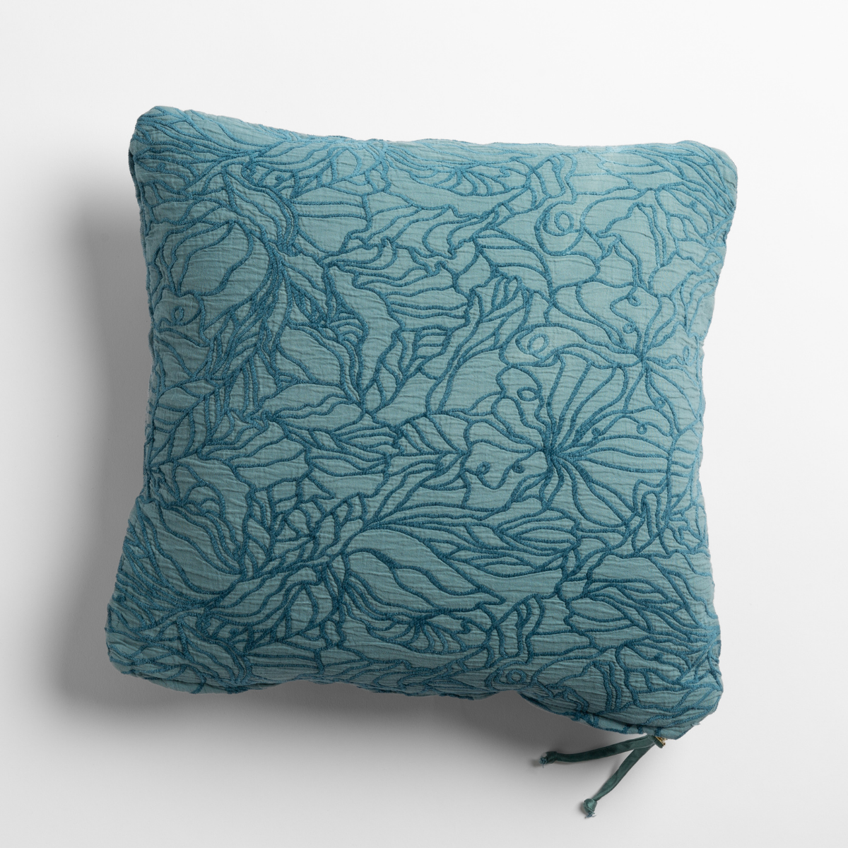 Cenote Georgia throw pillow, teal floral embroidery detail on textured fabric, corner ties visible.