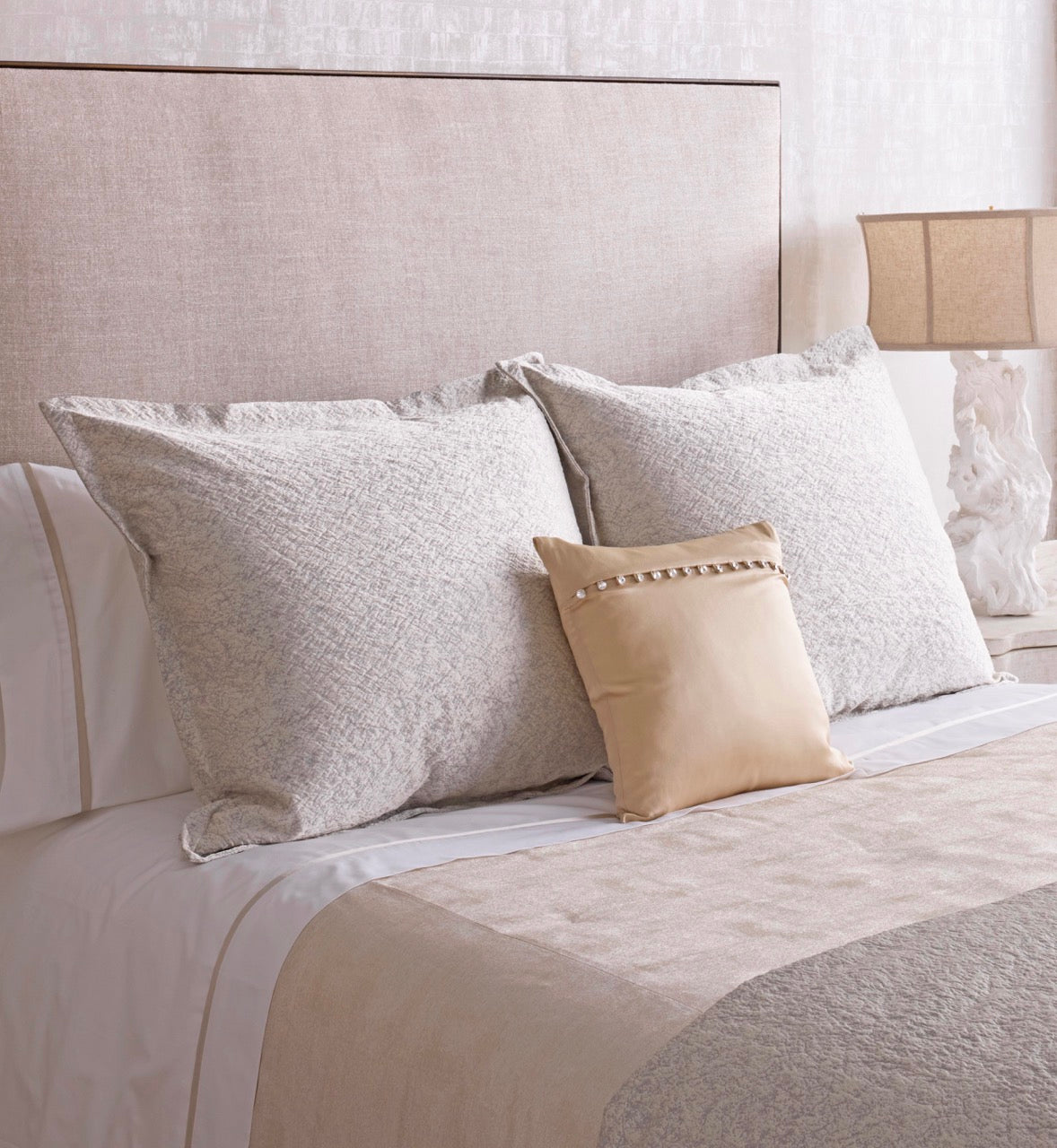 Glacier coverlet draped across bed, styled with textured ivory pillows and champagne accent cushion.