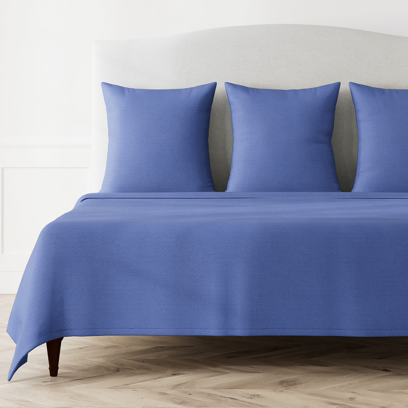 Periwinkle coverlet and matching pillow shams styled on a made bed in a bright white room.