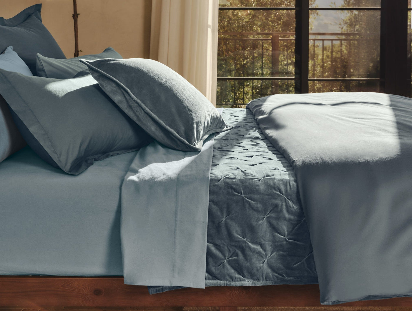 Close-up of Coyuchi Cloud Soft Sateen duvet cover in slate blue, styled on bed with matching pillows.