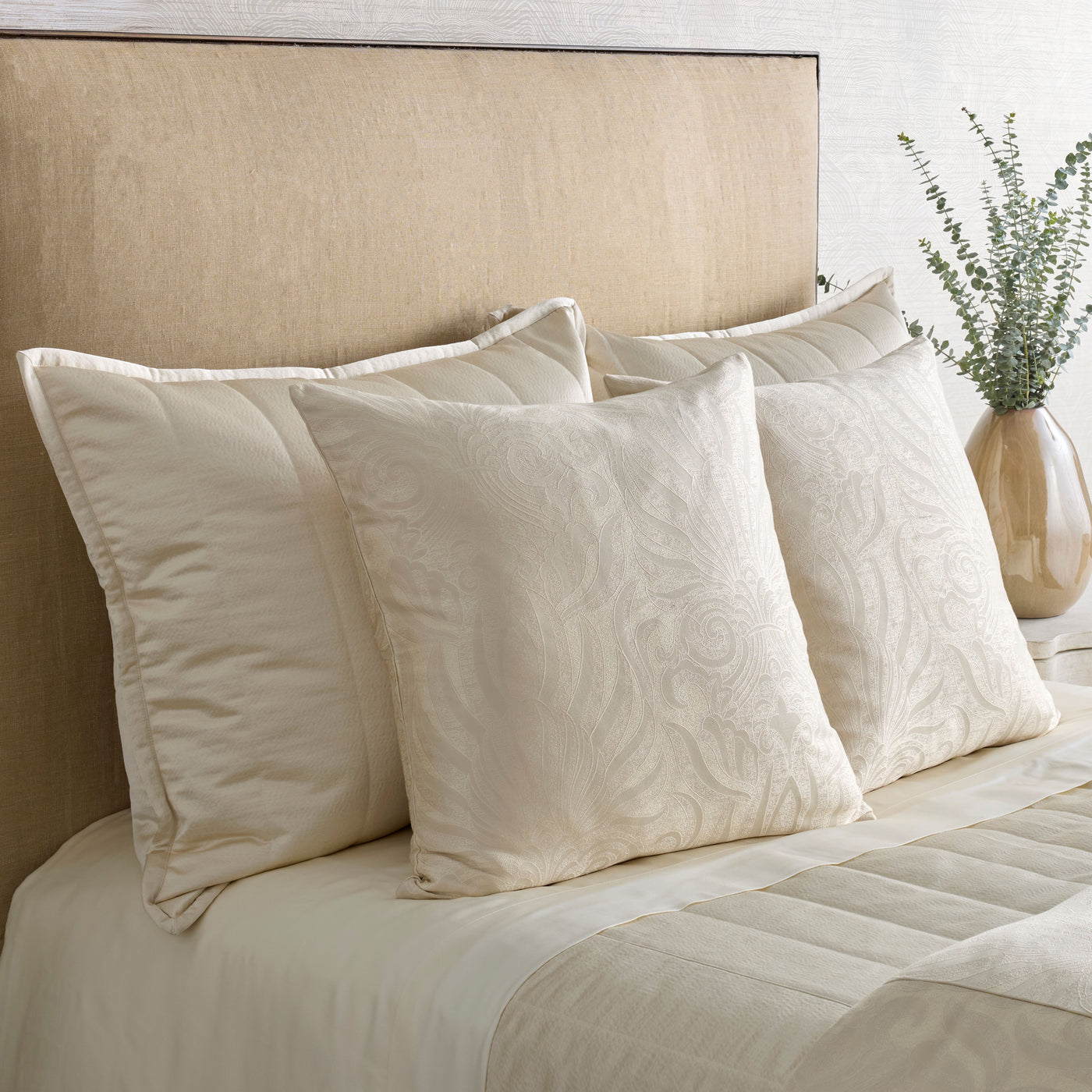 Close-up of ivory Ann Gish Hammered shams with floral texture, styled on a made bed.