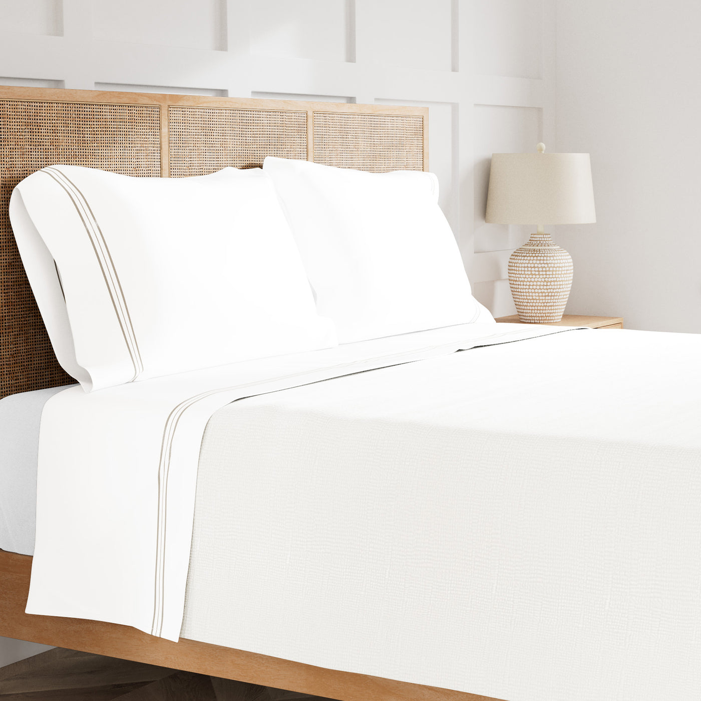 White sheet set styled on bed, featuring triple tan stitched stripe hem detail along flat sheet and pillowcases.