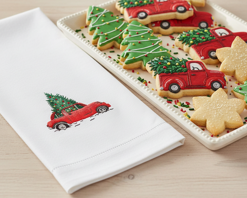 Decorative cookies shaped like red trucks and Christmas trees on a tray with a matching embroidered towel.