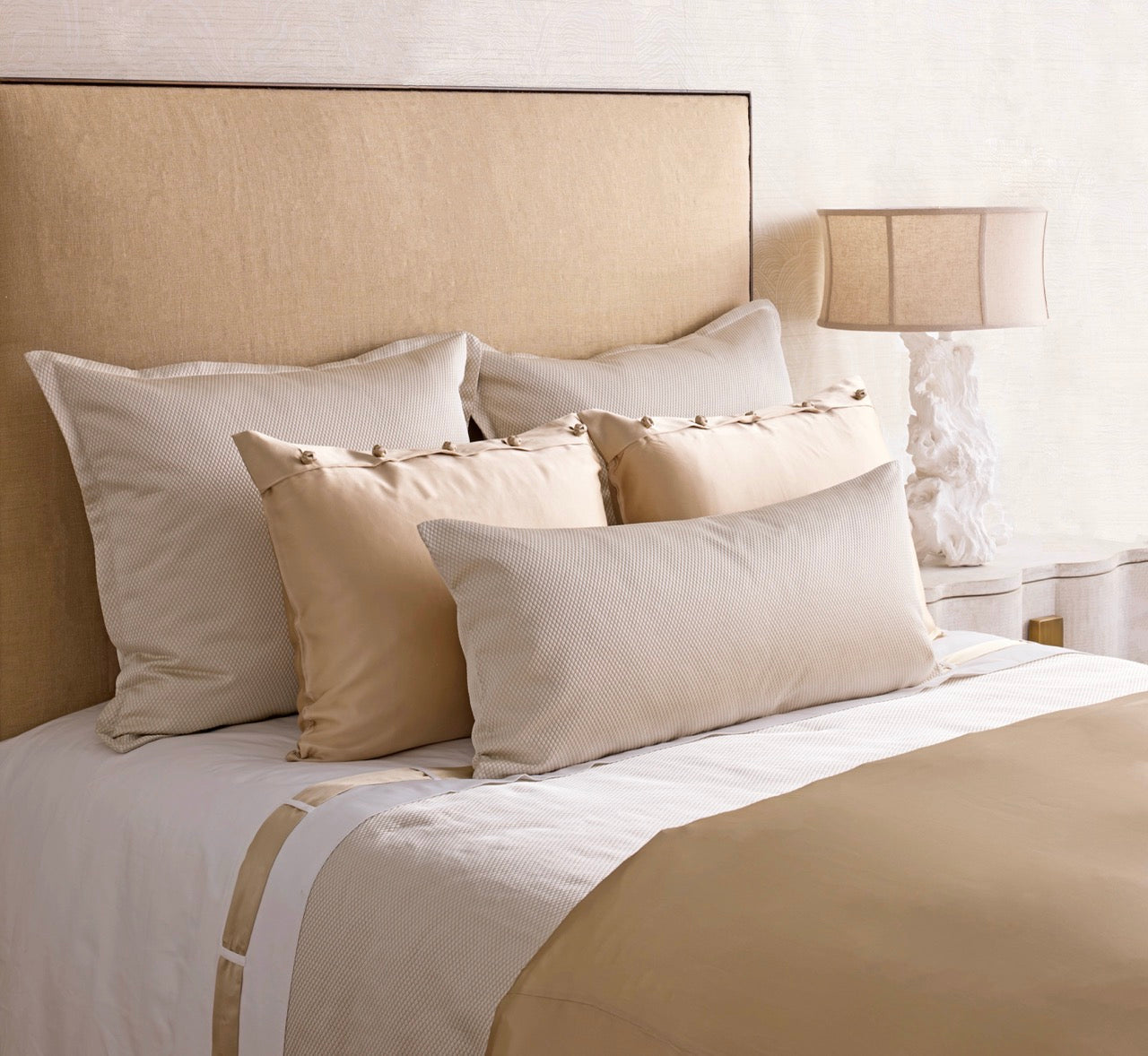 Champagne and ivory coverlet with layered pillow arrangement on styled bed.