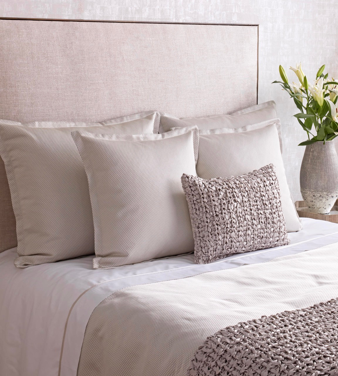 Neutral-toned bed styled with textured ivory coverlet, chunky knit accent pillow, and white floral arrangement.