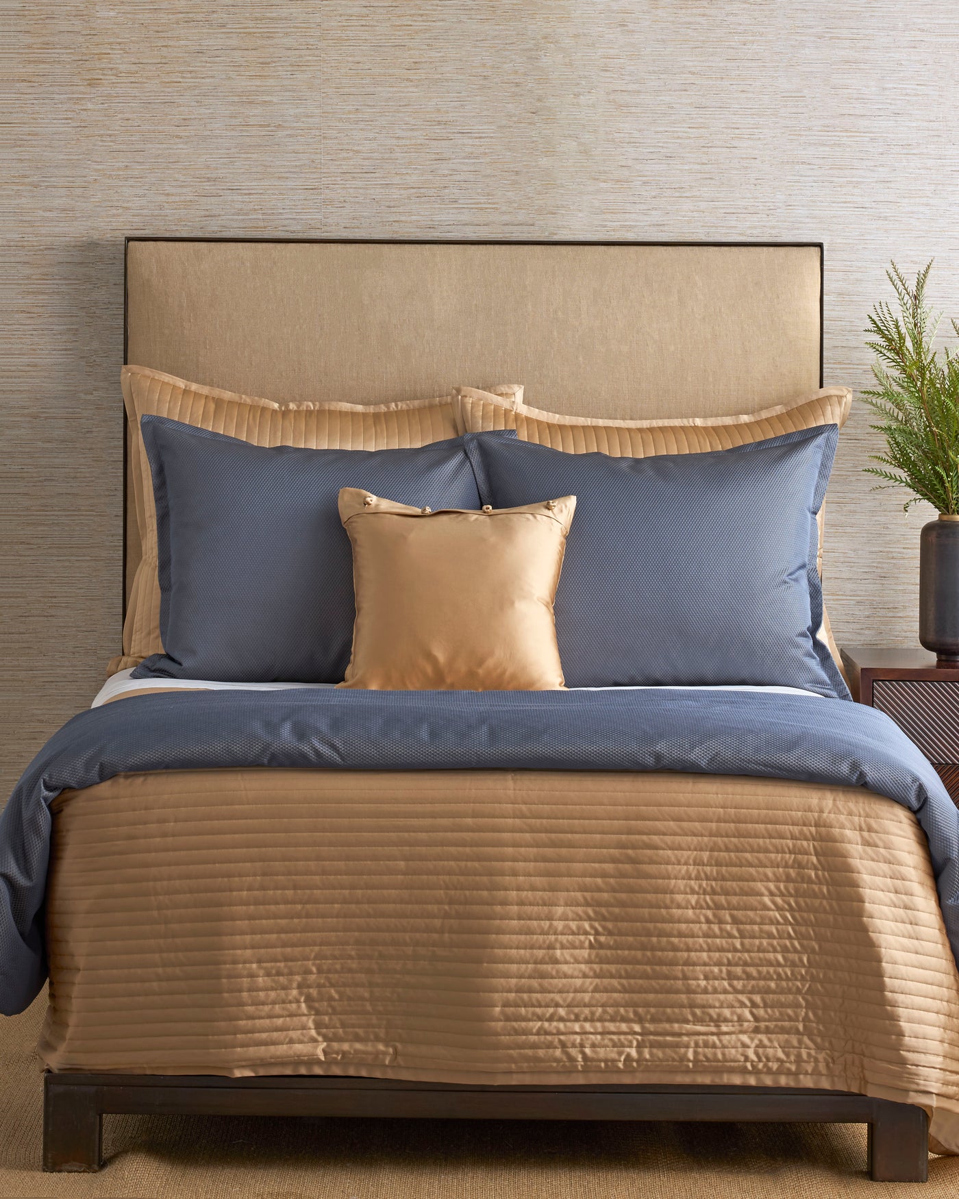 Champagne quilted coverlet styled on bed with slate blue Euro shams and gold accent pillow.