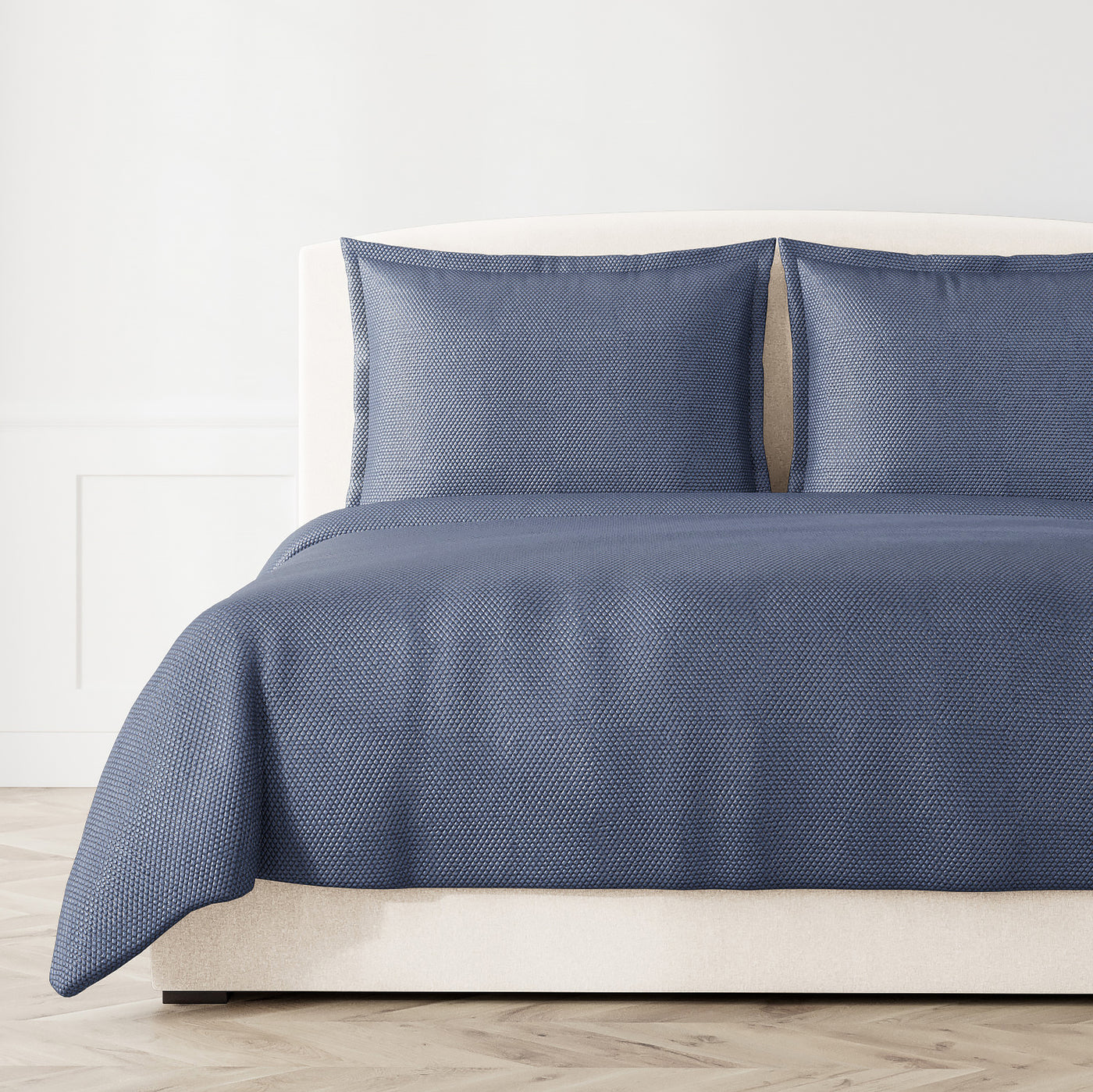 Ann Gish Hollywood coverlet in navy blue, styled on bed with matching shams, subtle woven texture.