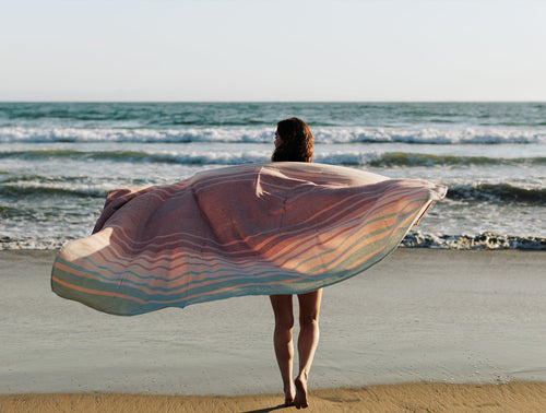 Coyuchi Laguna beach blanket held open in ocean breeze, multicolor stripe pattern, beach setting.