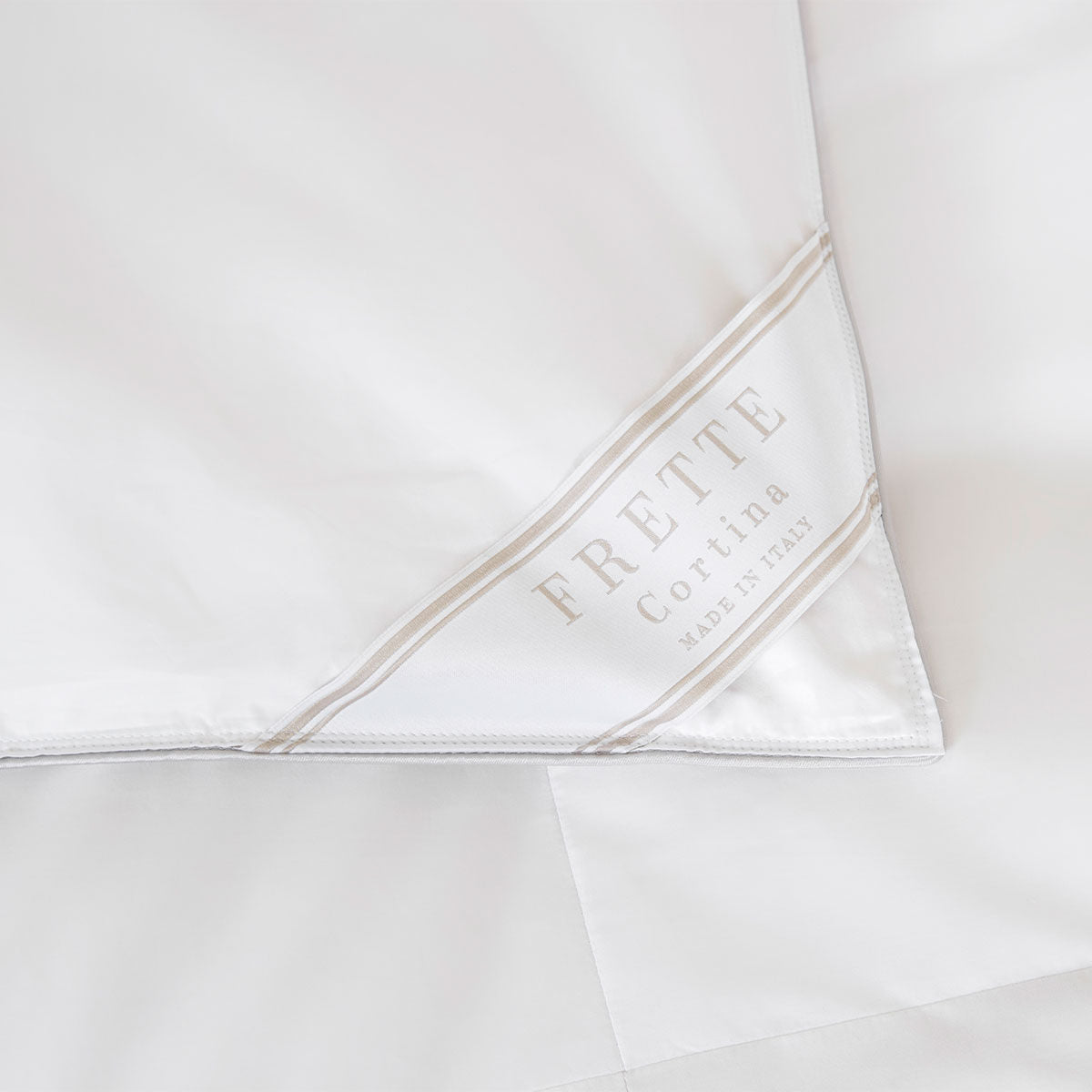 A close-up of the Cortina Down Duvet Insert by Frette, featuring a white cotton sateen cover and a corner label that reads "Frette Cortina Made in Italy" in beige text.