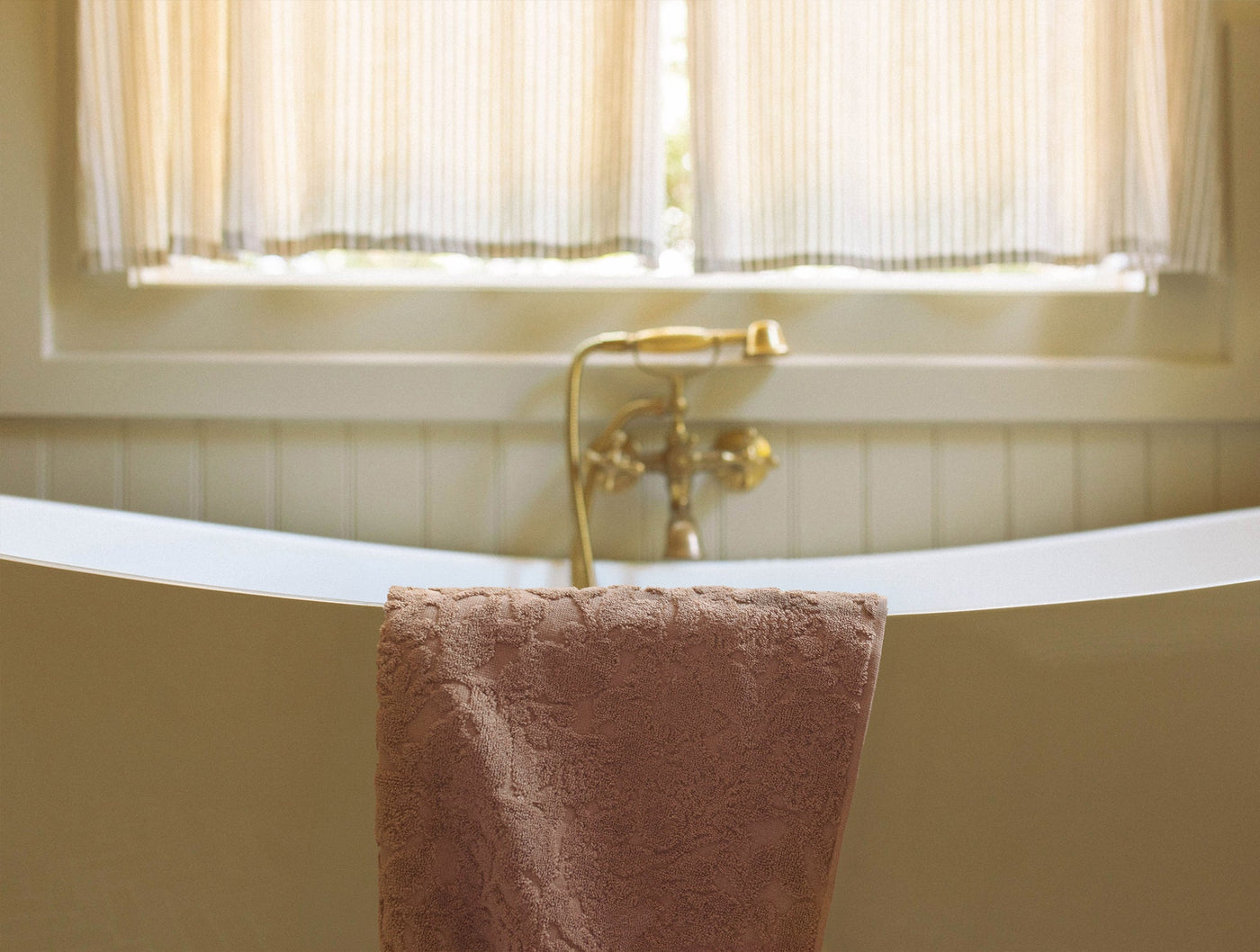 Blush Wildflower bath towel draped over a freestanding tub rim, brass fixtures behind.