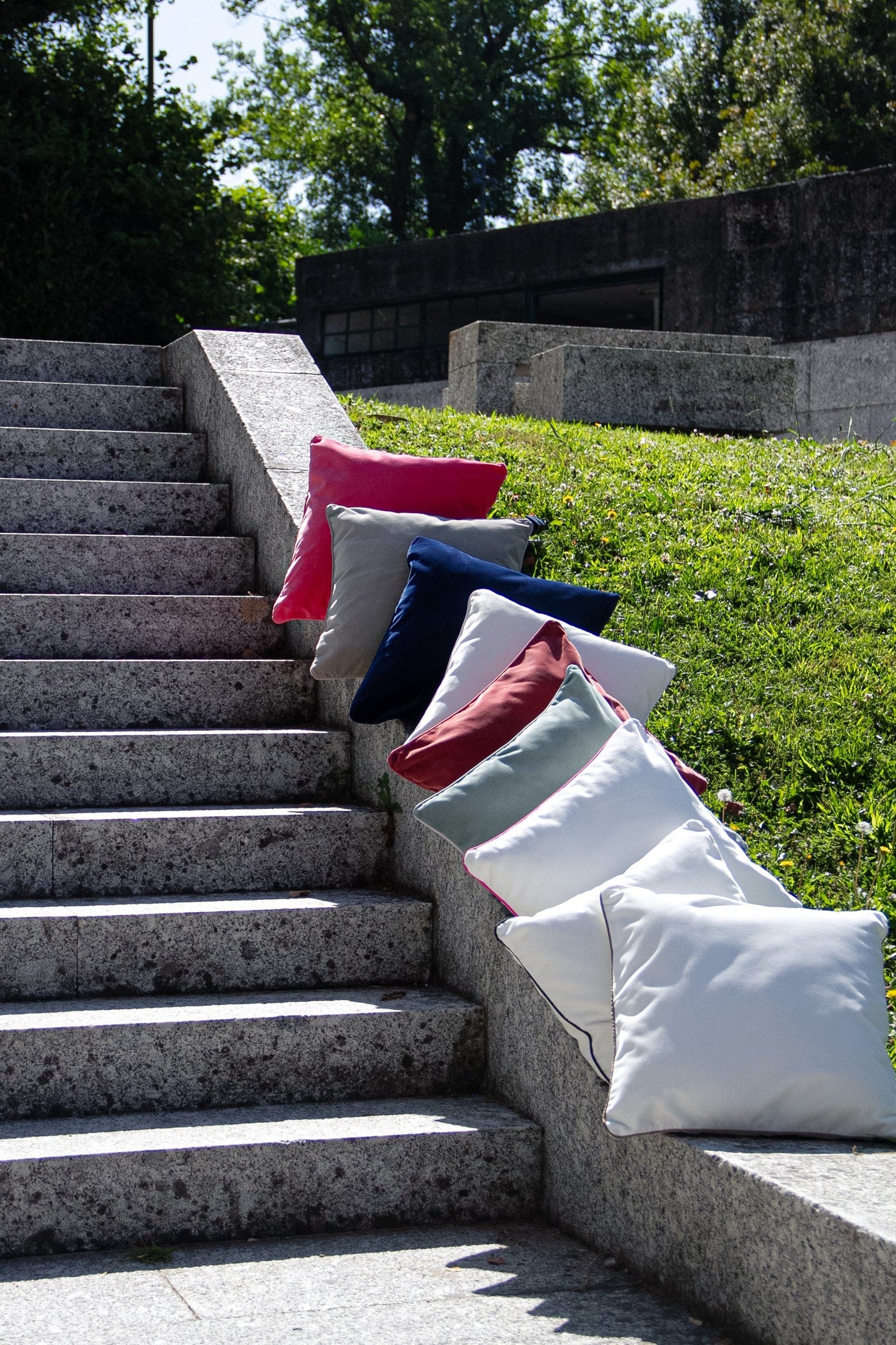 Colorful pillows arranged on a stone staircase with greenery in the background.