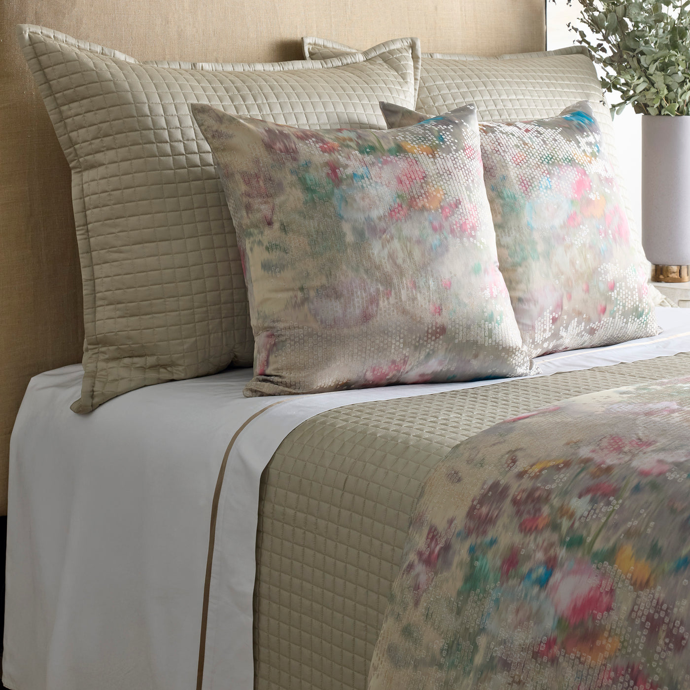 Watercolor floral euro pillow in pink, teal, and ivory tones against taupe quilted bedding.
