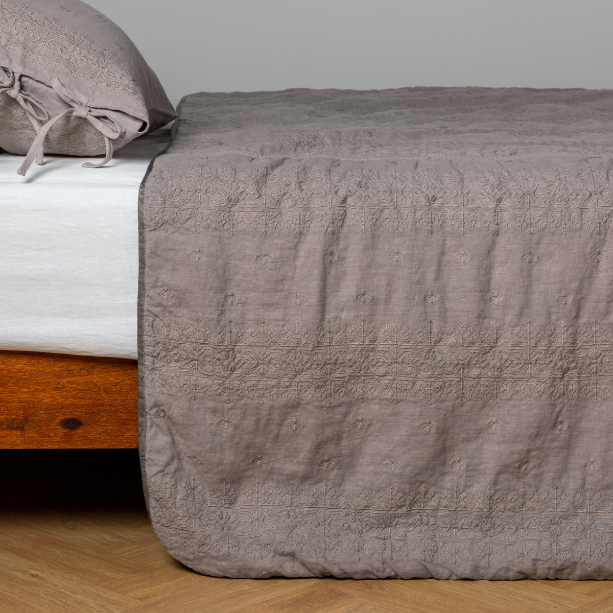 Bella Notte Ines bedspread in Fog draped over bed foot, showing quilted linen texture.