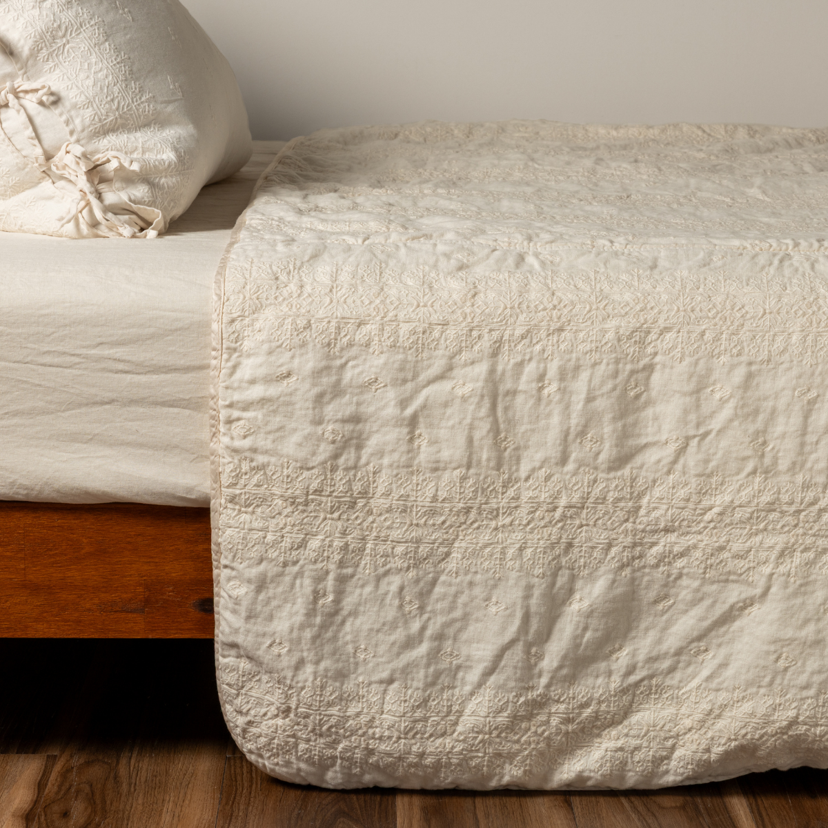 Bella Notte Ines bedspread in Natural, showing quilted foot drape over wood bed frame.