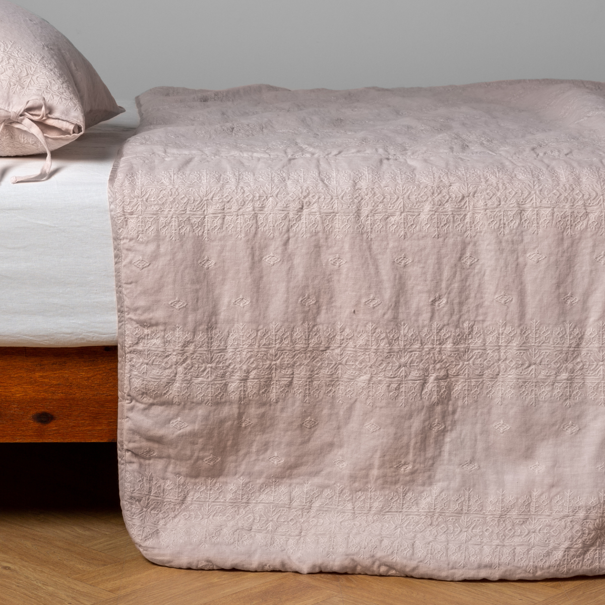Bella Notte Ines bedspread in Pearl draped over bed foot, showing embroidered border detail.