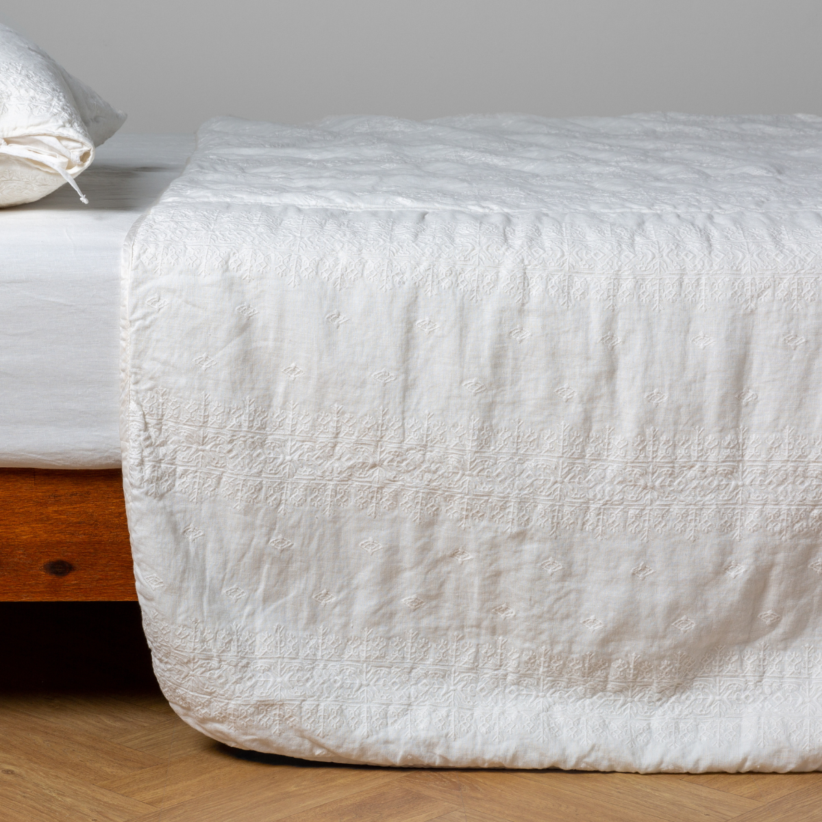 Bella Notte Ines bedspread in Winter White draped over bed foot, showing quilted linen texture.