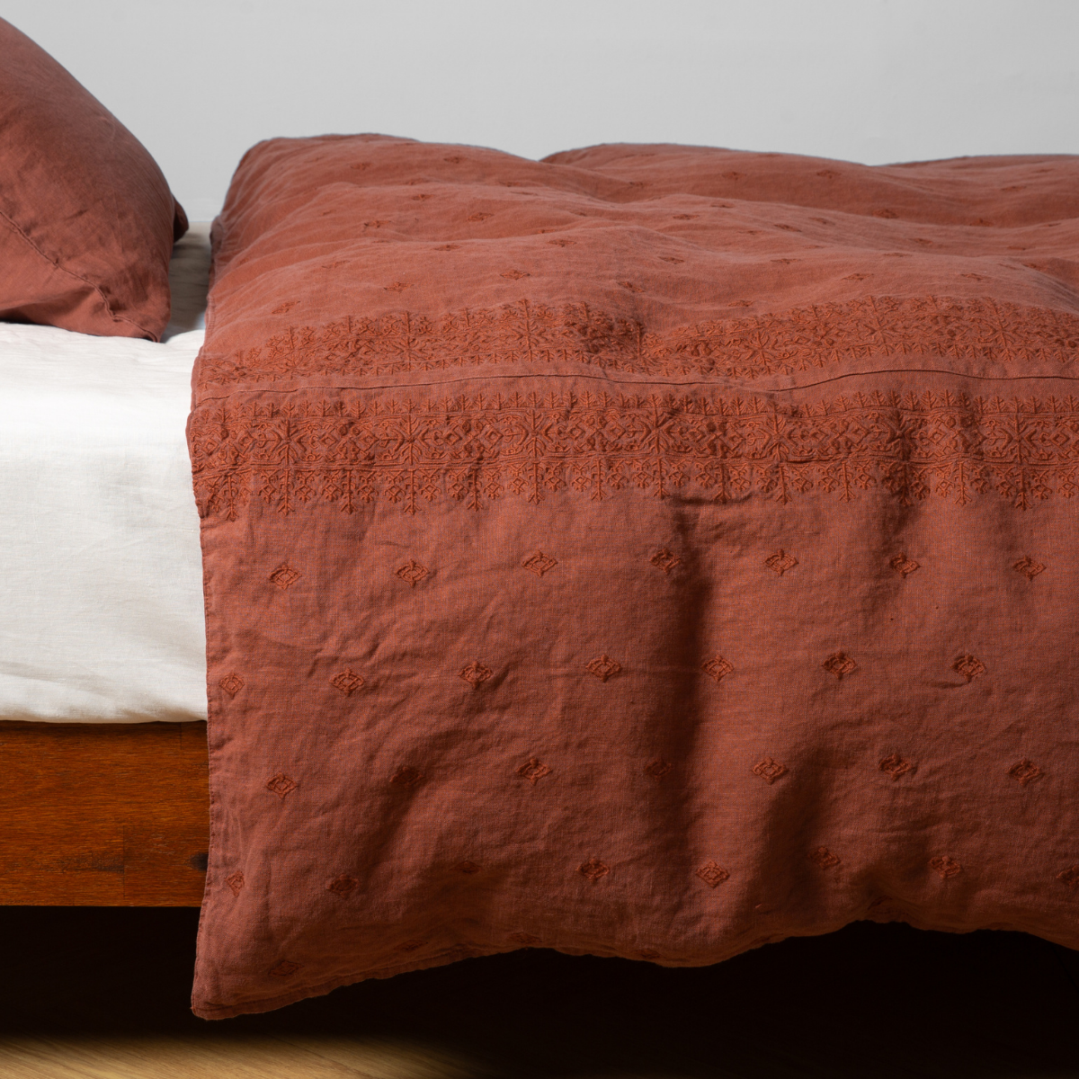 Autumn linen duvet cover draped over bed, tonal embroidered border detail visible at top edge.