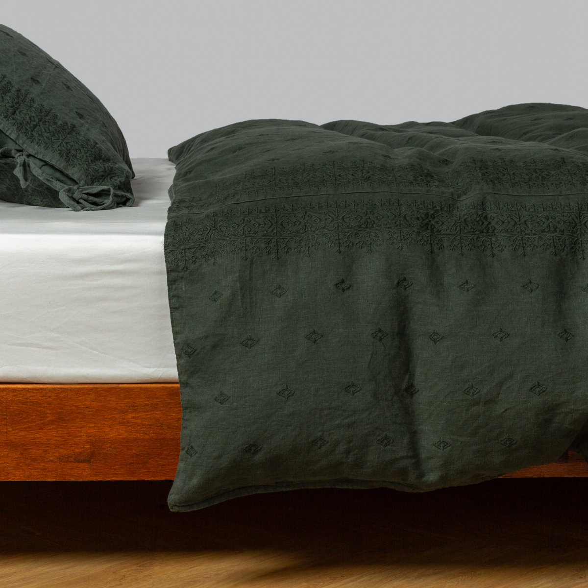 Dark Juniper Ines duvet draped over bed, tonal embroidered diamond pattern visible on linen.