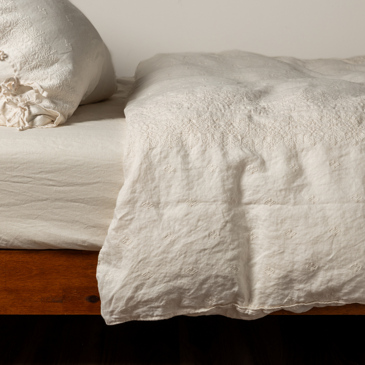 Natural Ines duvet cover draped over bed corner, showing relaxed linen texture on warm wood frame.