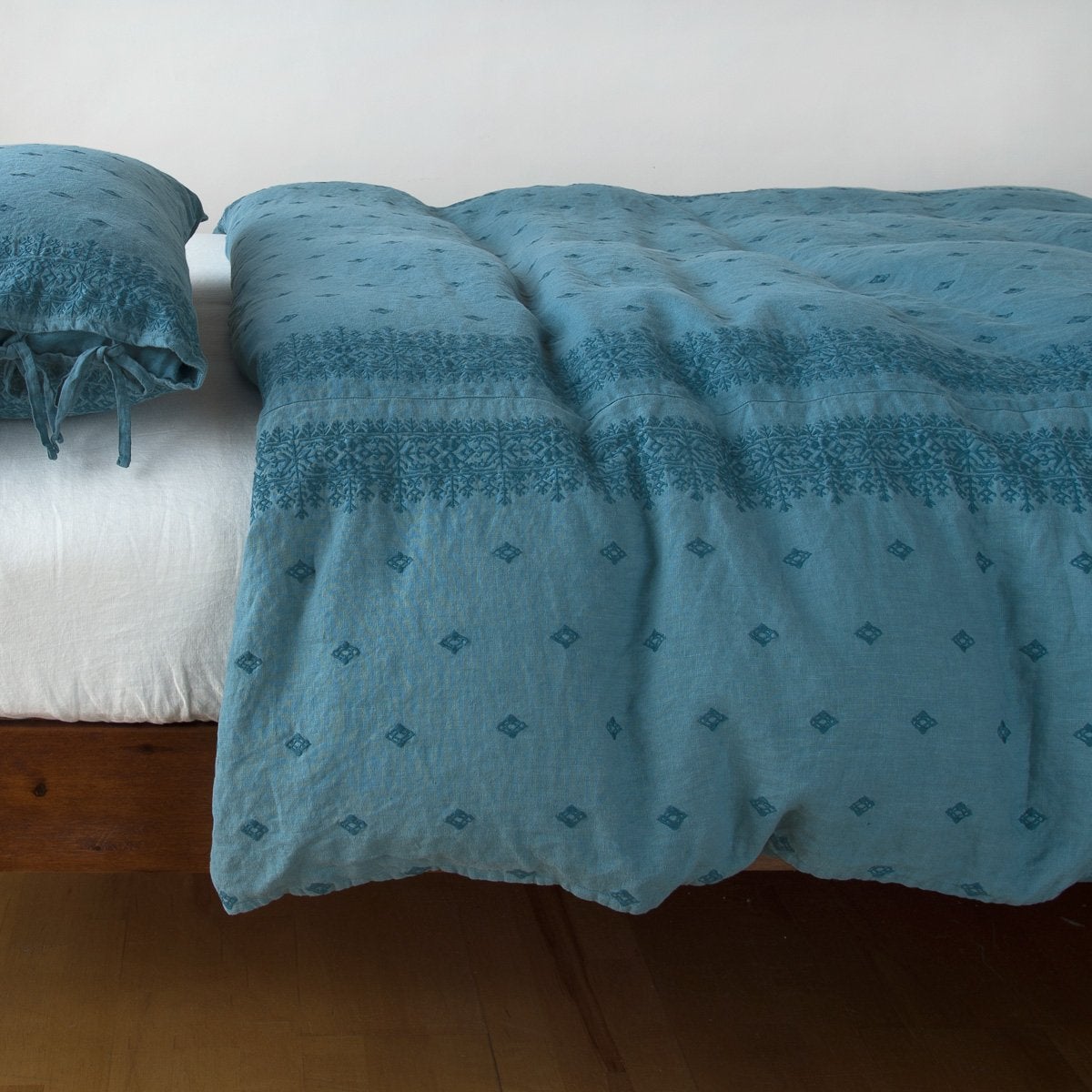 Bella Notte Ines duvet cover in Cenote draped over bed with matching pillow sham, geometric jacquard pattern visible.