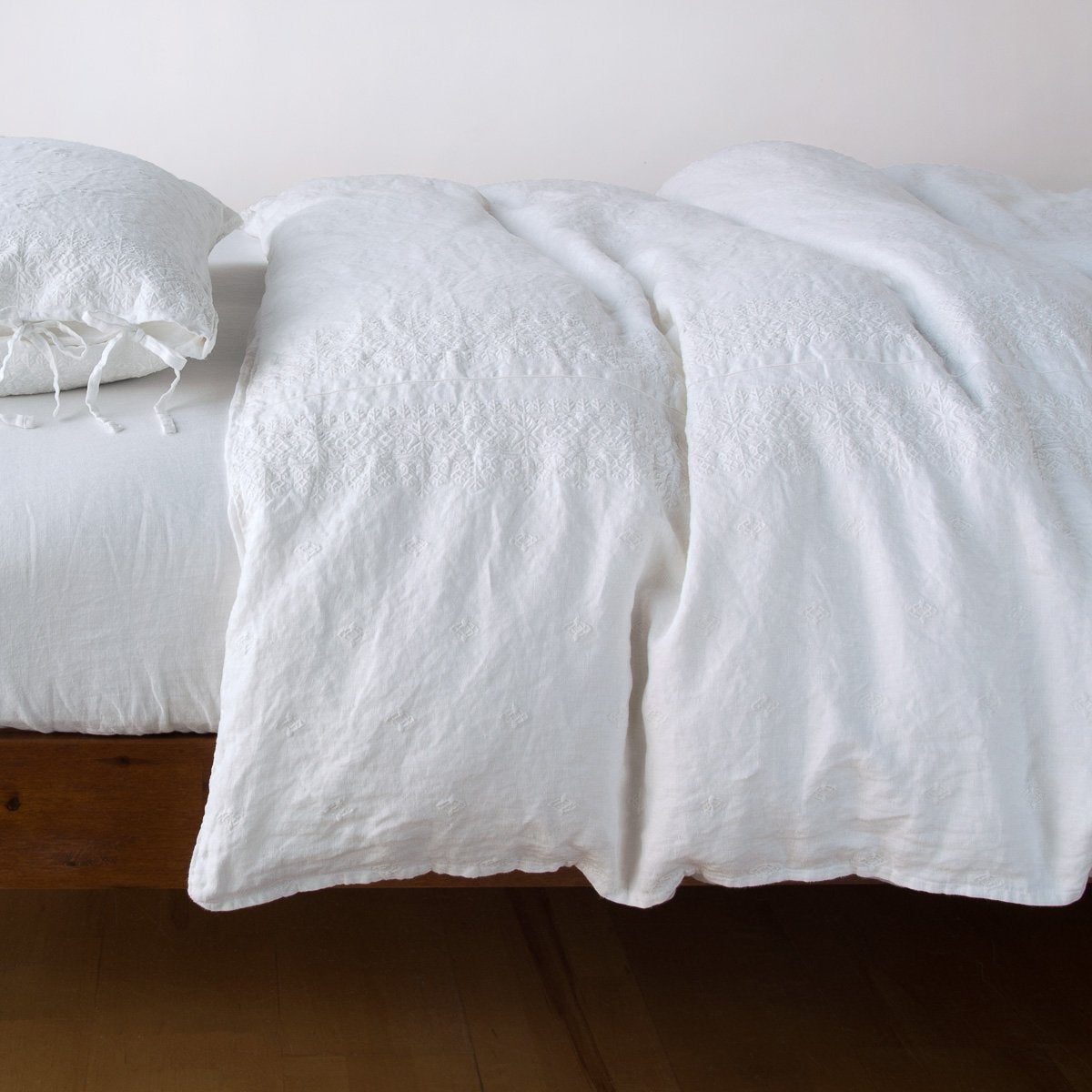 Bella Notte Ines duvet cover in White, relaxed linen draping over a low wood bed frame.