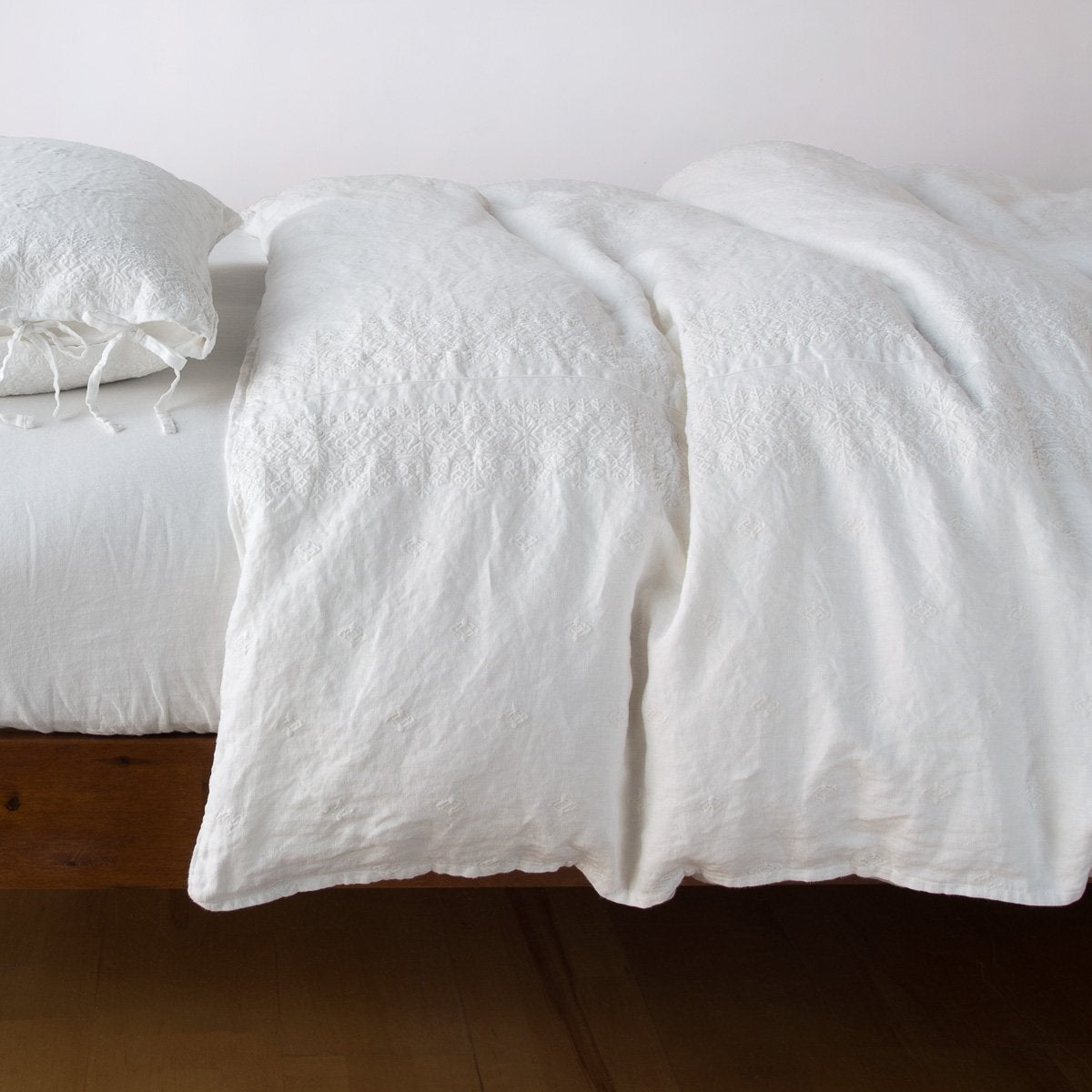 Bella Notte Ines duvet cover in Winter White, draped loosely over a low wood bed.