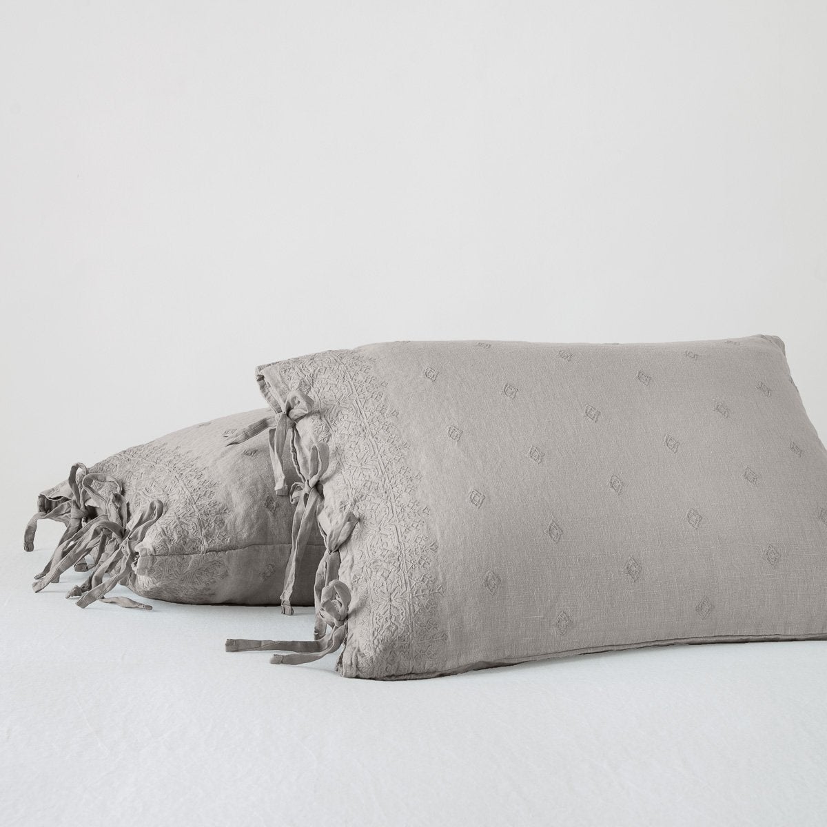 Two Bella Notte Ines shams in Fog, showing tied linen closures and tonal dot texture.
