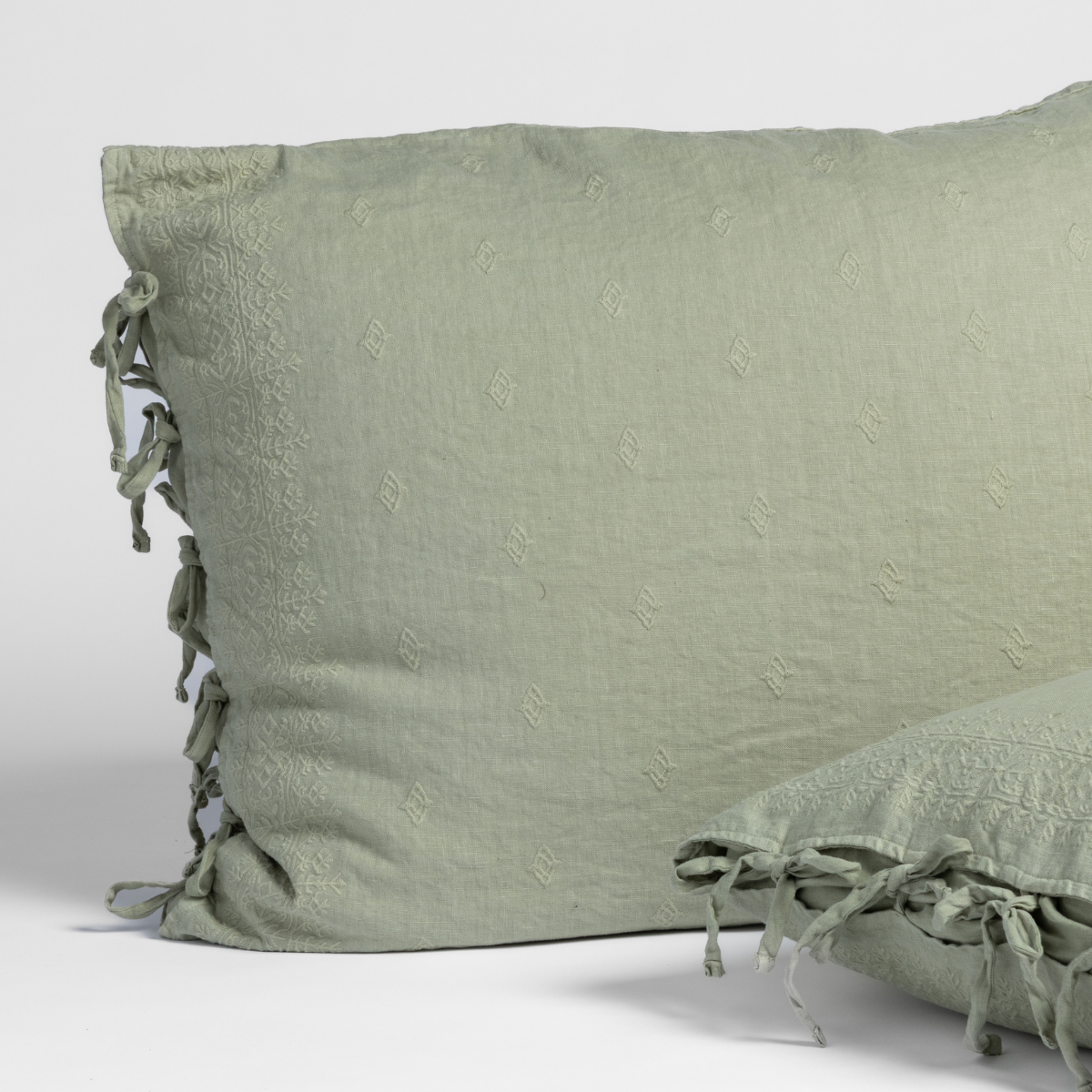 Close-up of Desert Sage Ines sham showing embossed texture and knotted tassel ties at side edge.