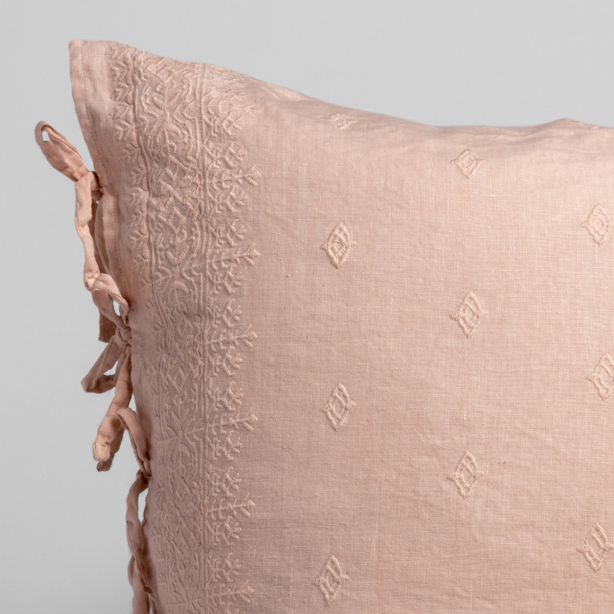 Close-up of Pearl linen sham with tonal embroidered border and ribbon ties at left edge.