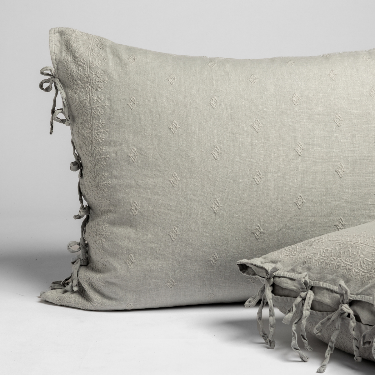 Sage-toned linen Ines shams in Cloud with tone-on-tone monogram embroidery and ribbon tie closures.