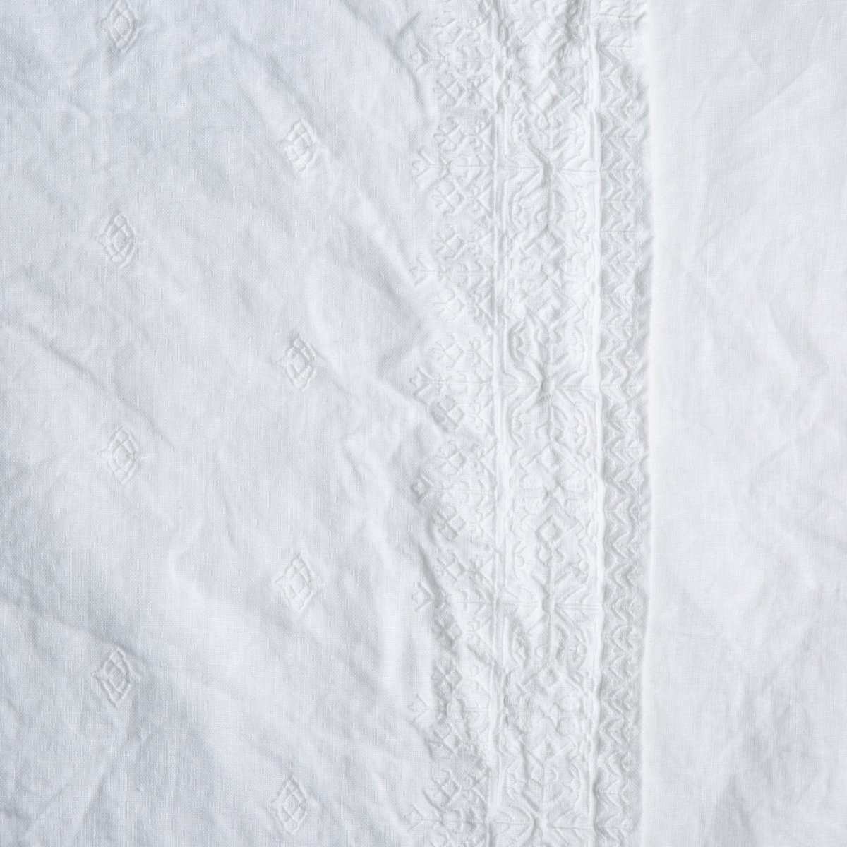 Close-up of white linen sham with tonal geometric embroidery border and diamond motif details.