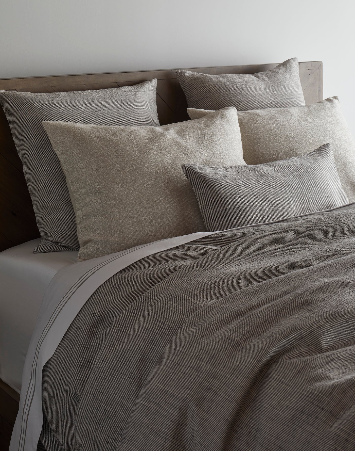 Angled view of charcoal textured linen duvet cover styled with layered natural and grey pillows.