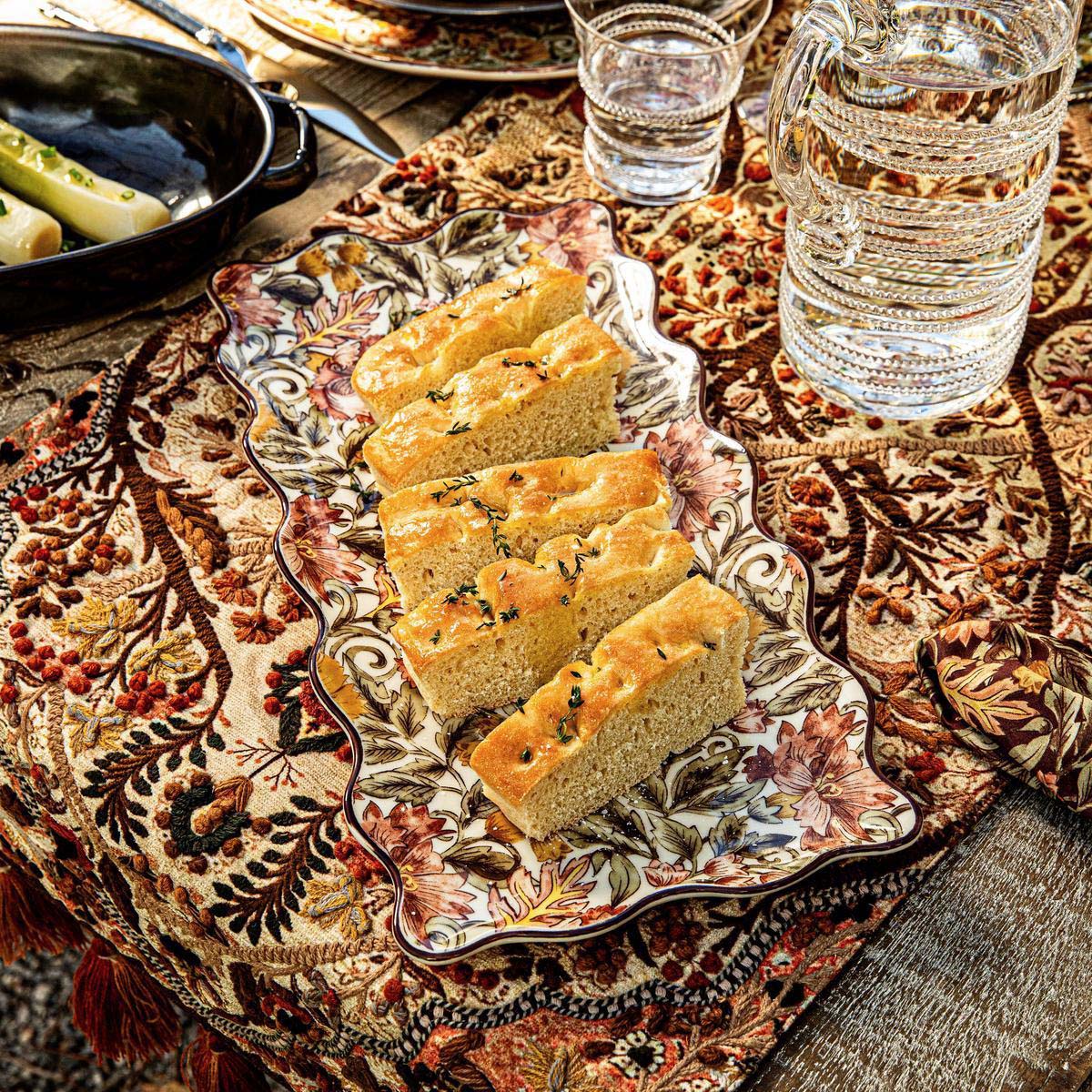 Juliska Willa hostess tray of focaccia on an embroidered runner beside a glass pitcher
