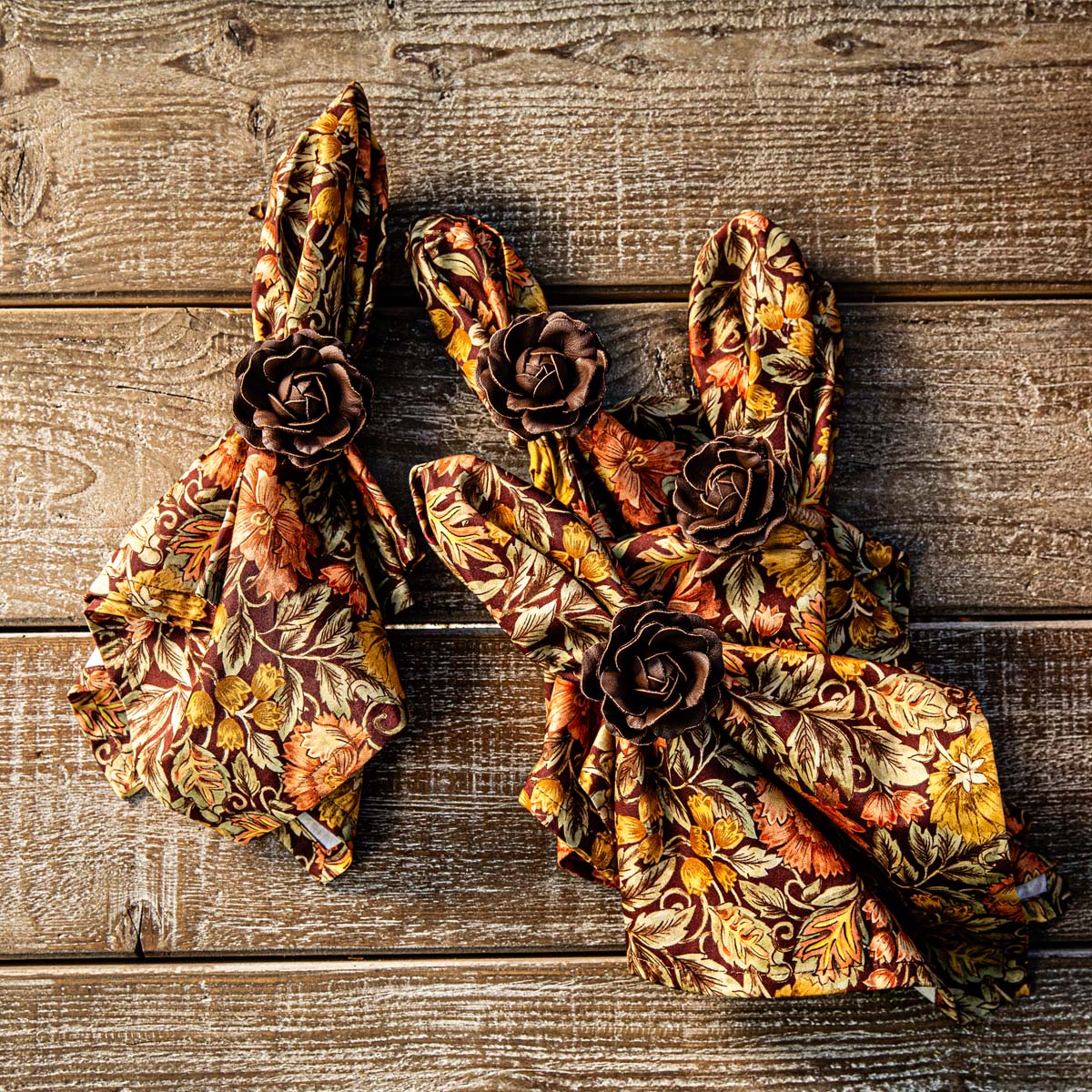 Three Juliska Willa napkins gathered in rose napkin rings on a weathered wood table