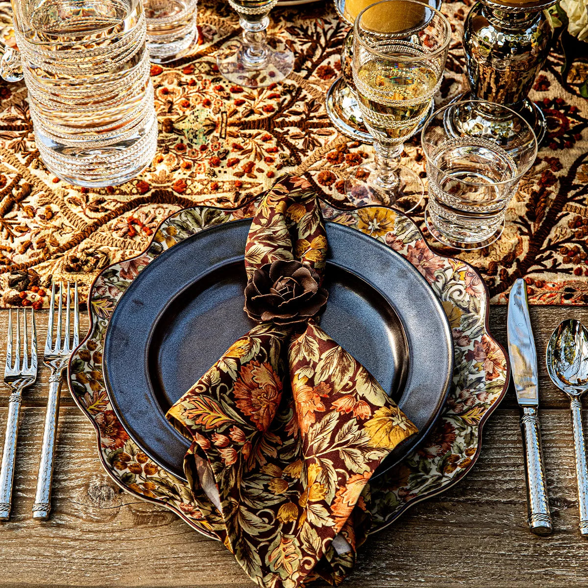 Juliska Willa floral napkin tucked in a rose napkin ring on a dark charger at a set table