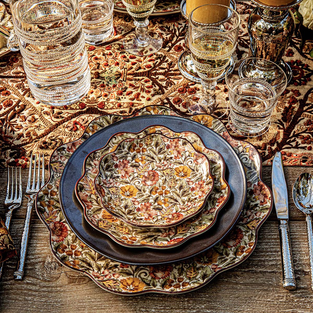 Juliska Willa place setting of a scalloped salad plate on a dark charger over the Willa platter, on an embroidered runner with glassware