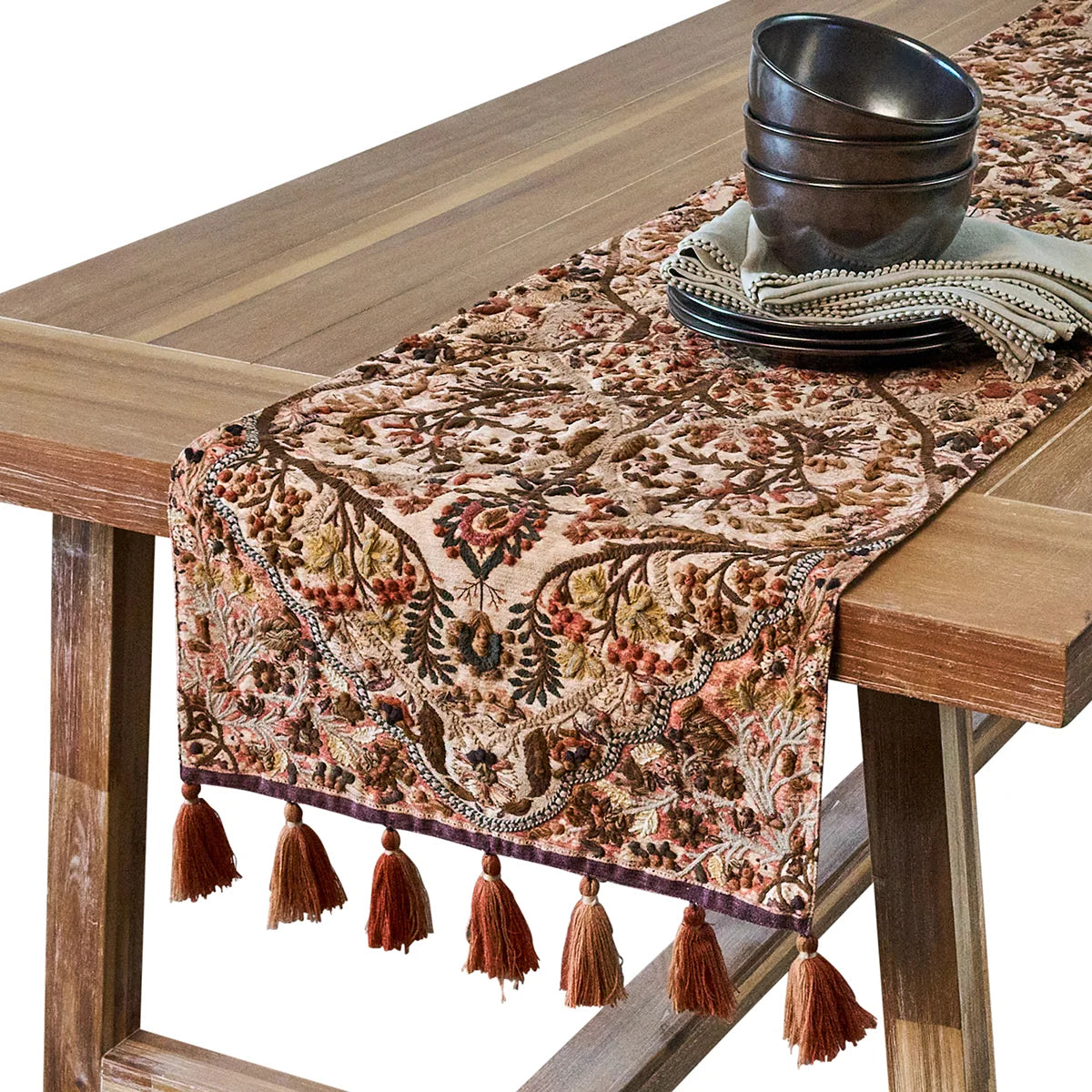 Juliska Willa embroidered runner over a wooden table end with tassels hanging, dark bowls stacked on top