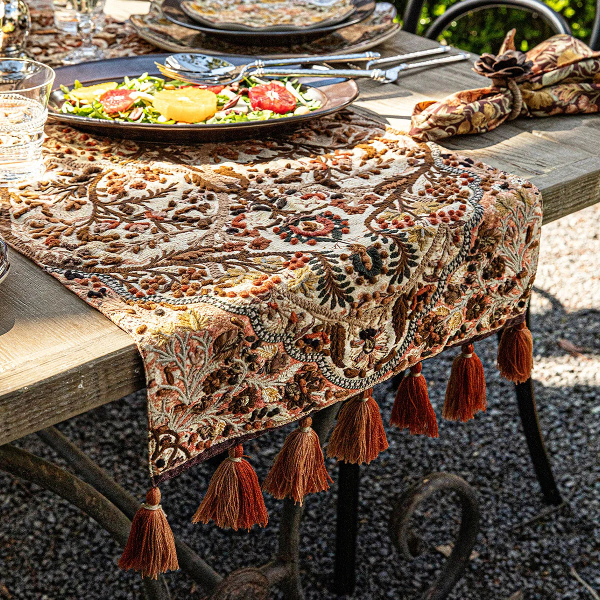 Juliska Willa embroidered runner with rust tassels on an outdoor table set for a meal
