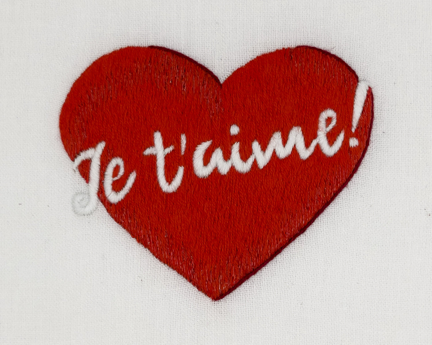 Close-up of red embroidered heart with white Je t'aime script on ivory linen.