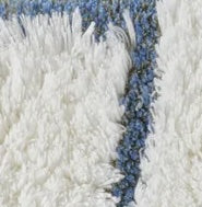 Close-up of ivory shag bath rug with cornflower blue border detail.