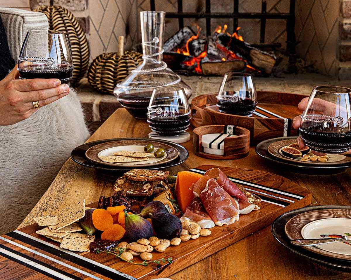 People enjoying a meal with wine and charcuterie by a fireplace.