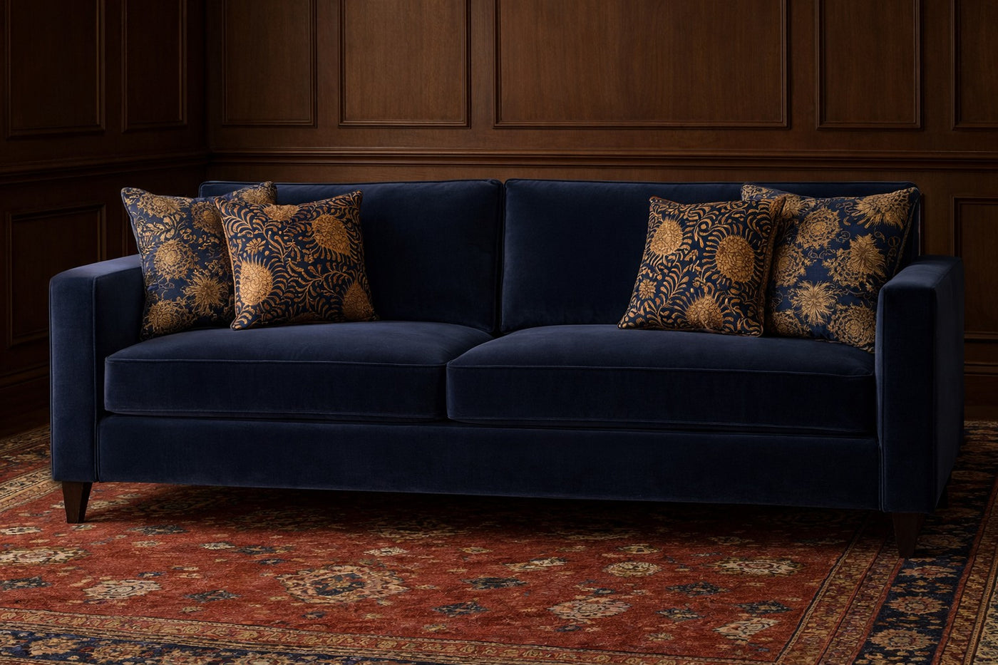 Navy and gold floral euro shams styled on a deep blue velvet sofa in a wood-paneled room.