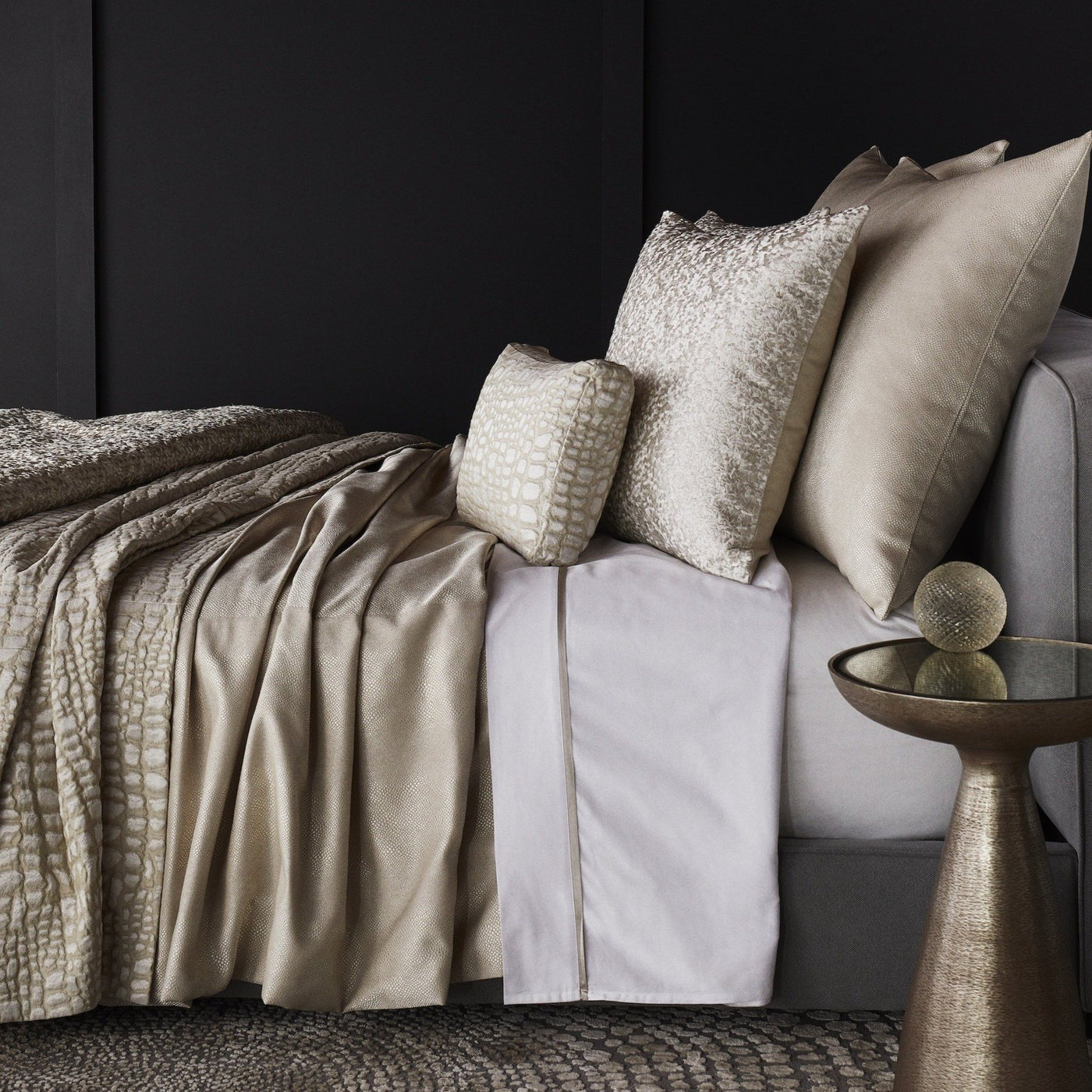 Champagne textured coverlet and pillows styled on a bed with white sheets and gold accents.